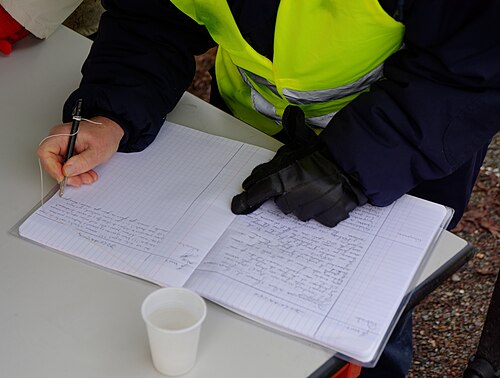 Un manifestant en gilet jaune écrit sur un cahier de doléances posé sur une table.