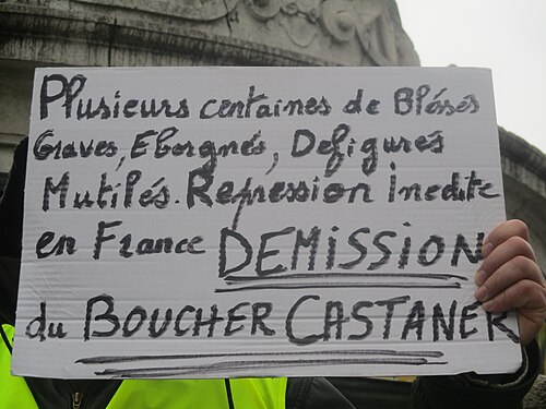 Pancarte manuscrite « Plusieurs centaines de blessés graves, éborgnés, défigurés, mutilés. Répression inédite en France. Démission du boucher Castaner ».