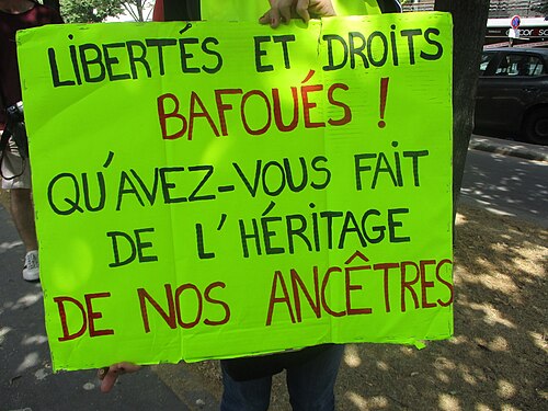 Pancarte verte « Libertés et droits bafoués, qu'avez-vous fait de l'héritage de nos ancêtres ? ».