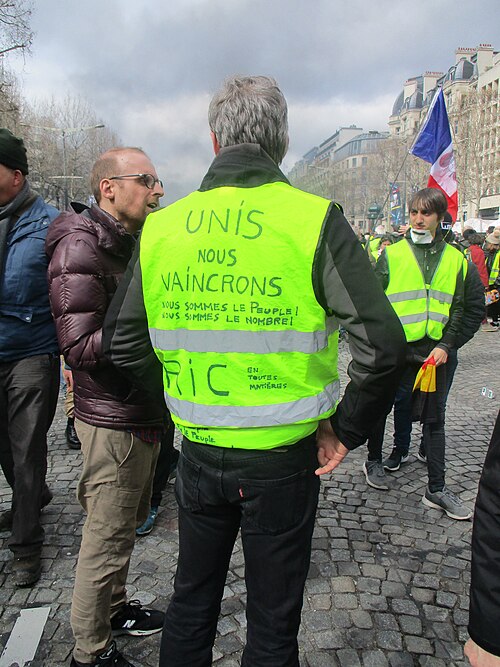 Deux manifestants portant des gilets annotés « Unis nous vaincrons » et « RIC ».